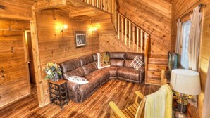 A wooden interior with a curved leather sofa, a small table with a vase, and a lamp. - Three Bears Cabin- Enjoy the scenery around you with a peaceful view (Sautee Nacoochee)