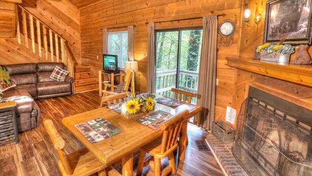 A wooden cabin interior with a dining table, chairs, a fireplace, a television, and a staircase. - Three Bears Cabin- Enjoy the scenery around you with a peaceful view (Sautee Nacoochee)