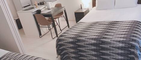Habitación de hotel con cama, escritorio y silla. Hay un microondas y una tetera sobre el escritorio.