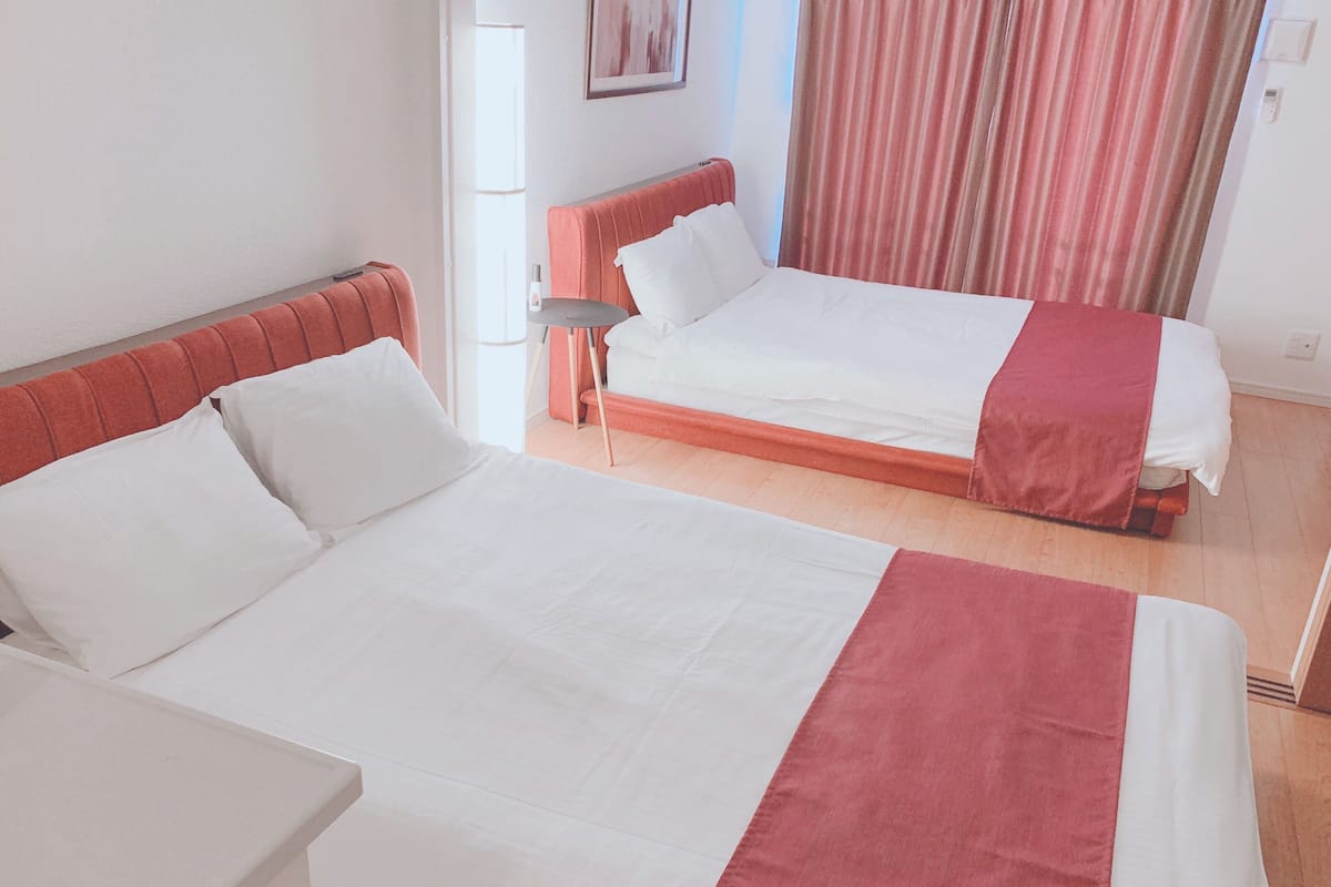 A hotel room with two beds, a small table, and a window with curtains.