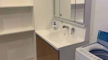 A modern bathroom with a white sink, a mirror, a built-in washing machine, and wooden cabinets.