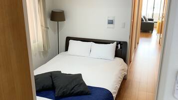 A hotel room with a bed, a bedside table, a lamp, a thermostat, and a control panel.