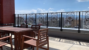 Un balcón con una mesa y sillas de madera, barandilla de metal decorativa y vista panorámica de la ciudad.