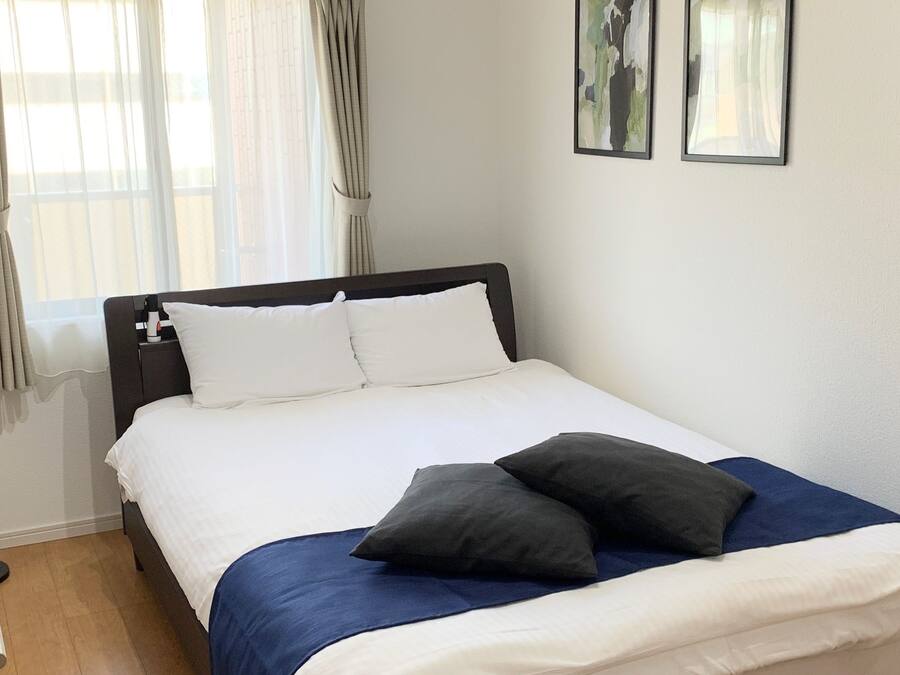 Una cama bien tendida con almohadas blancas y oscuras, una colcha azul y suelo de madera.