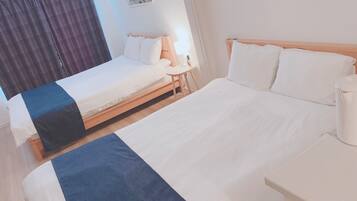 A hotel room with two beds, a bedside table with a lamp, and a window with curtains.