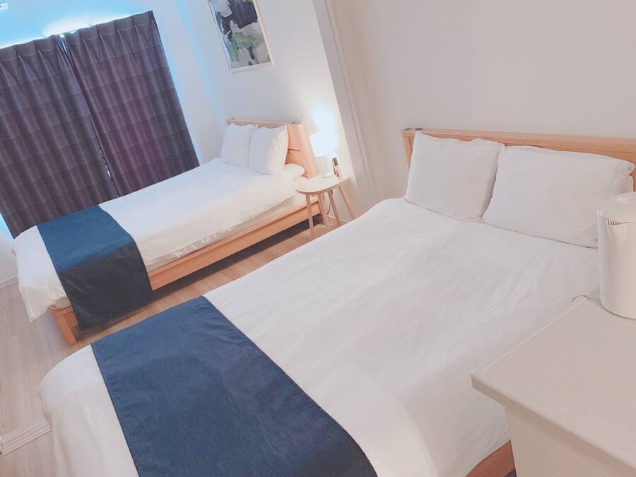 A hotel room with two beds, a bedside table with a lamp, and a window with curtains.