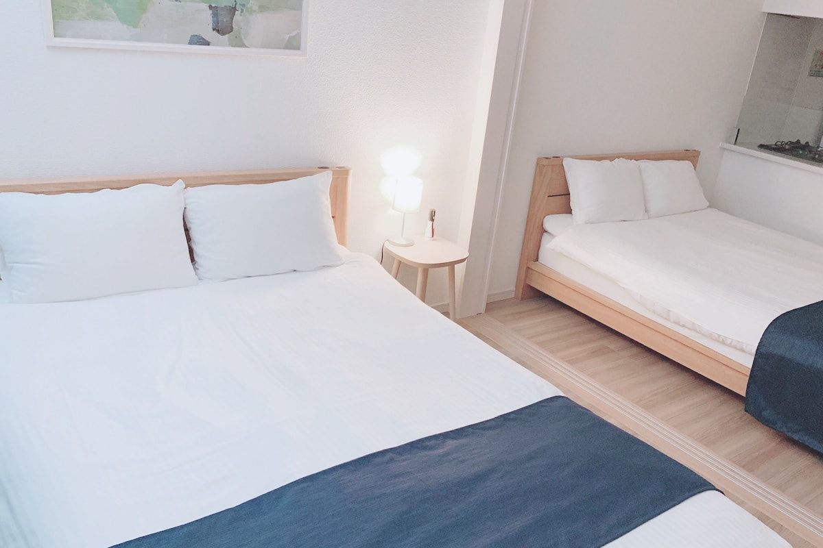 A hotel room with two beds, a small bedside table with a lamp, and a painting on the wall.