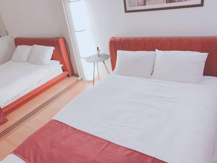 Two single beds with white linens and red headboards in a room with a tiled floor.