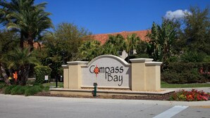 A sign for Compass Bay with a clear view of the surrounding greenery and a building with a red-tiled roof in the background. - New Listing! Compass Bay Resort, 3mi to Disney & 9mi to Universal - IT3006 (Kissimmee)