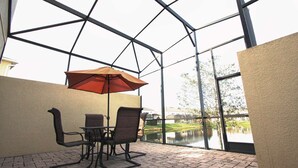 A glass-enclosed patio with a table and chairs, an umbrella, and a view of a lake. - New Listing! Compass Bay Resort, 3mi to Disney & 9mi to Universal - IT3006 (Kissimmee)