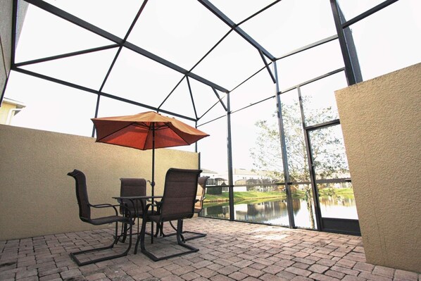 A glass-enclosed patio with a table and chairs, an umbrella, and a view of a lake.