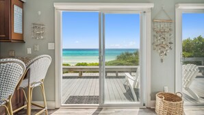 Een kamer met uitzicht op het strand, een eethoek met rieten stoelen en een decoratieve wanddecoratie.