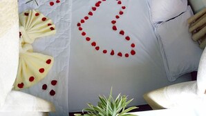 Un lit surmonté d’un arrangement en forme de cœur composé de pétales de roses rouges, disposés sur l’oreiller.