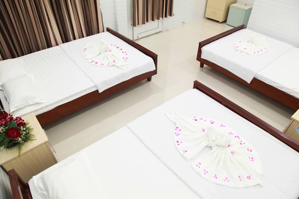 Habitación de hotel con cuatro camas, cada una con una toalla y pétalos de flores rosas dispuestos sobre ellas.