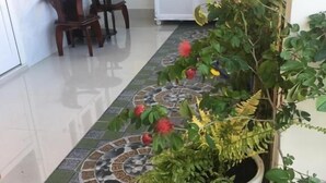 Un couloir doté d’un sol carrelé, d’une plante en pot, d’une armoire et d’un coin repas avec des chaises et une table.