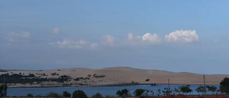 A desert landscape with sand dunes, a body of water, and sparse vegetation.