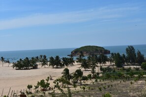 A beach with palm trees, a small hut, and a rocky outcrop in the distance.