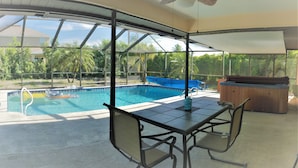 A covered outdoor area with a pool, a hot tub, and a table with chairs. - VILLA THERESA -Tropical Paradise home Perfect for Family or a Romantic Vacation (Cape Coral)
