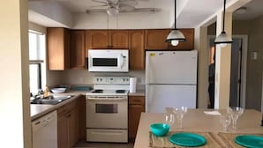 A kitchen with wooden cabinets, a microwave, a stove, a refrigerator, and a dining area with a table set for two. - VILLA THERESA -Tropical Paradise home Perfect for Family or a Romantic Vacation (Cape Coral)