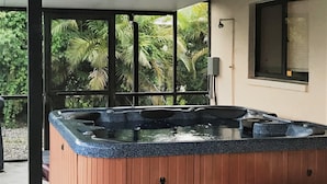 A hot tub with a wooden exterior and a black countertop, located under a covered area with a window and a view of palm trees. - VILLA THERESA -Tropical Paradise home Perfect for Family or a Romantic Vacation (Cape Coral)