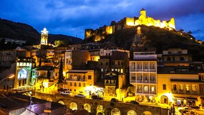 Un castell històric en un turó amb vista a una vila amb edificis il·luminats i un pont.