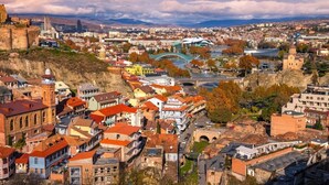 Un paisatge urbà històric amb una fortalesa destacada, un riu amb un pont, i una combinació d'arquitectura tradicional i moderna.