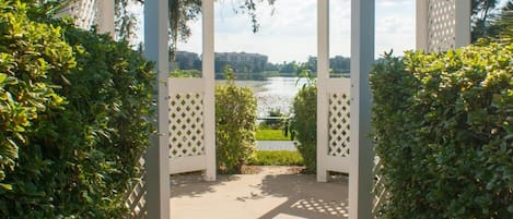 Una estructura de pérgola blanca con diseño de celosía, rodeada de follaje y que da a una vista de agua.