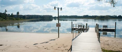 A wooden dock leading to a calm lake with a 'NO SWIMMING' sign, surrounded by trees and a clear sky.