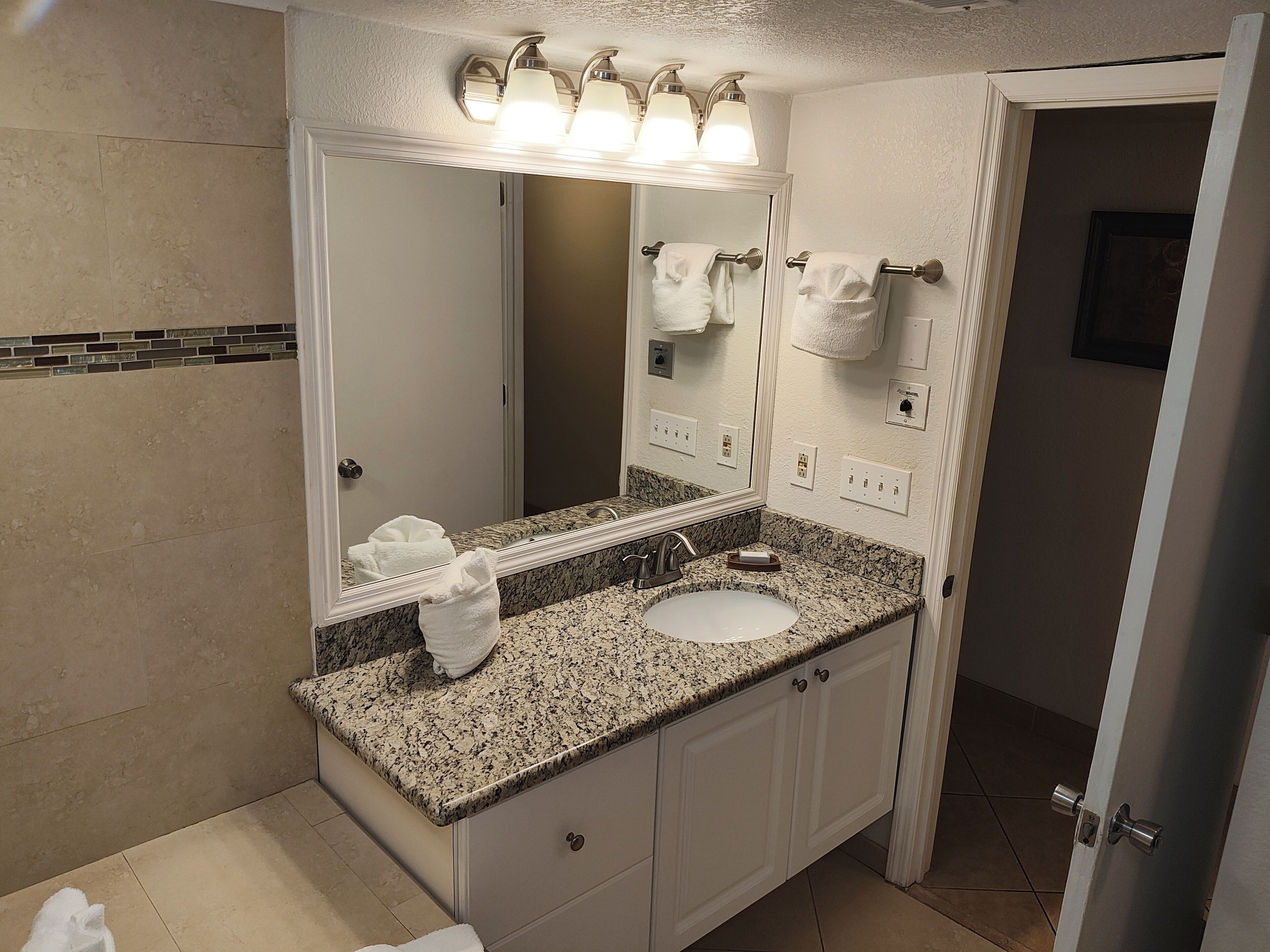 A bathroom with a granite countertop, a white sink, a large mirror, and a towel rack with towels.