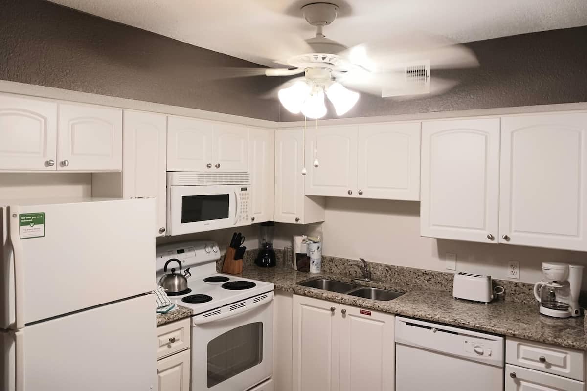 A kitchen with white cabinets, a microwave, stove, sink, and a ceiling fan.