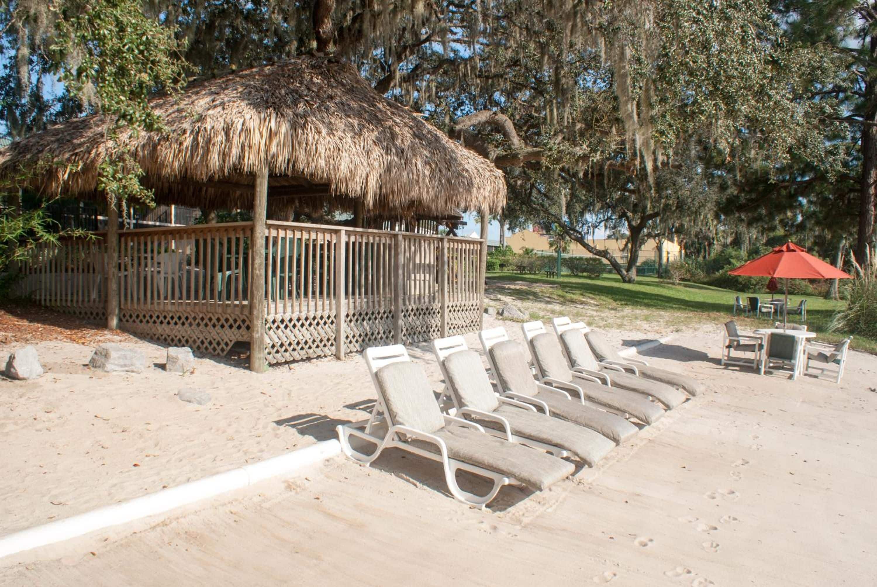 A beach area with a thatched structure, lounge chairs, and a red umbrella.