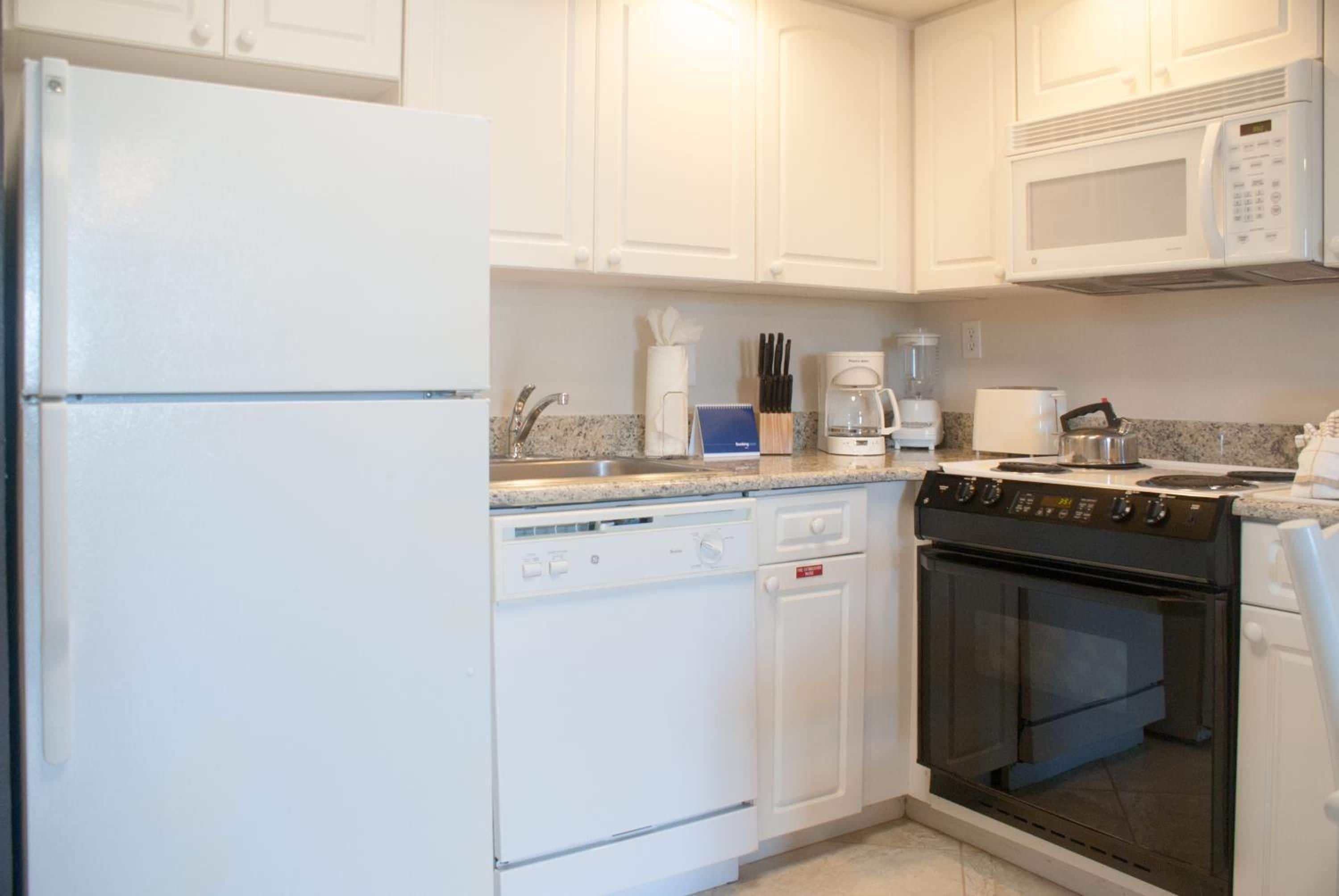 A kitchen with white cabinets, a dishwasher, a stove, a microwave, and a coffee maker.