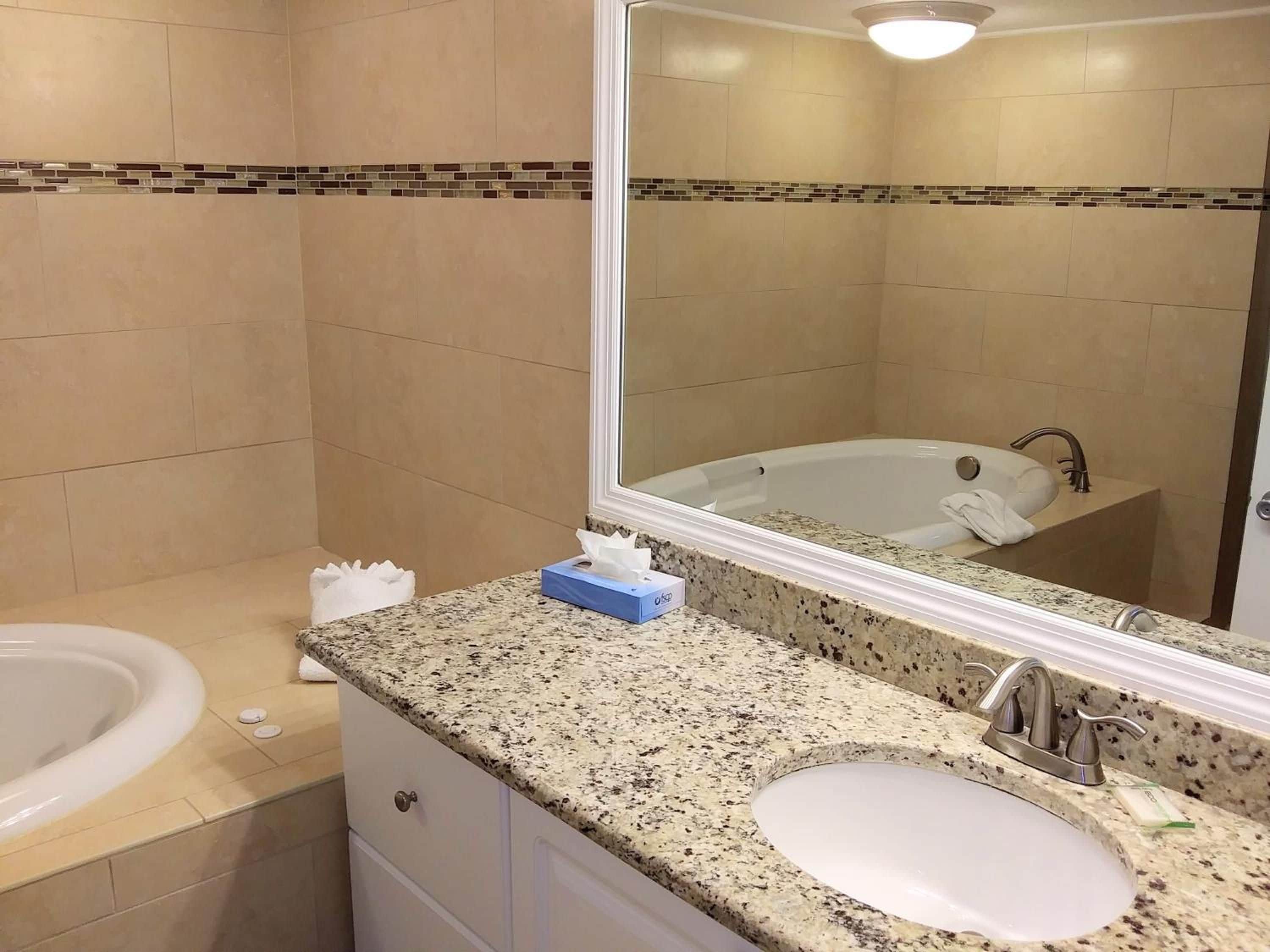 A bathroom with a granite countertop, a sink, a bathtub, and a mirror.