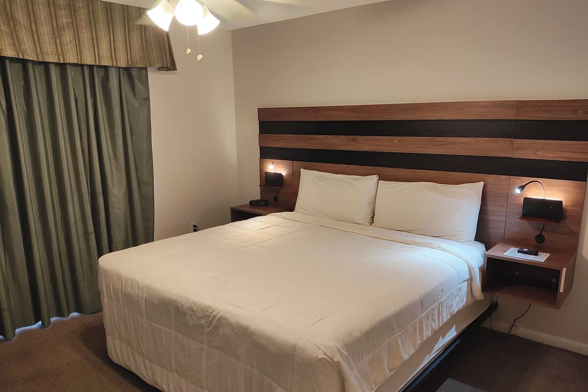 A hotel room with a large bed, wooden headboard, two bedside tables with lamps, and a curtain on the window.