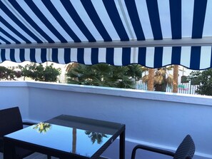 Un balcon agrémenté d’un auvent à rayures, d’une table en verre et de chaises.
