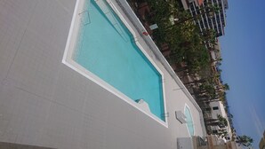 Una piscina con bordeado de baldosas, rodeada de edificios y palmeras.