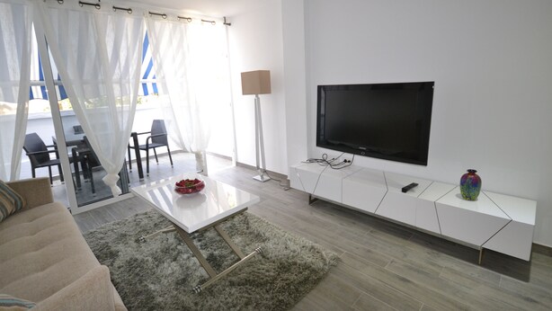 Una sala de estar moderna con un televisor de pantalla plana, muebles blancos y vistas al exterior.