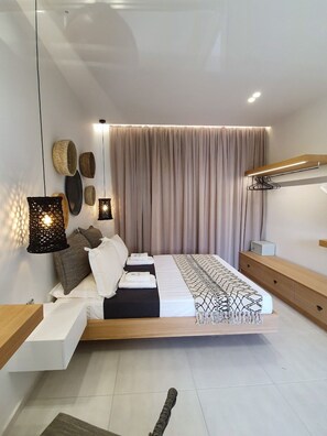 A modern bedroom with a bed, bedside tables, a hanging light fixture, and a large window with curtains. - St Thomas Beach Luxury Apartments (Rhodes)