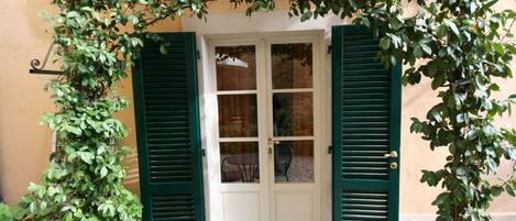 Una puerta con contraventanas verdes, un cristal y una pequeña mesa con una silla al frente.