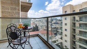 A balcony with a table and chairs, a clear view of the cityscape, and a building with a stone facade.