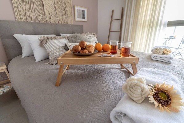 Een net opgemaakt bed met een dienblad vol gebak, een kop thee en een zonnebloem decoratie.