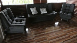Una habitación con un sofá de cuero negro, un sillón a juego y una butaca capitonada. El suelo es de madera y hay ventanas grandes con vistas a zonas verdes.