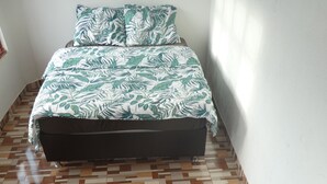 Un dormitorio con una colcha estampada, un sofá negro y un suelo de madera a cuadros.