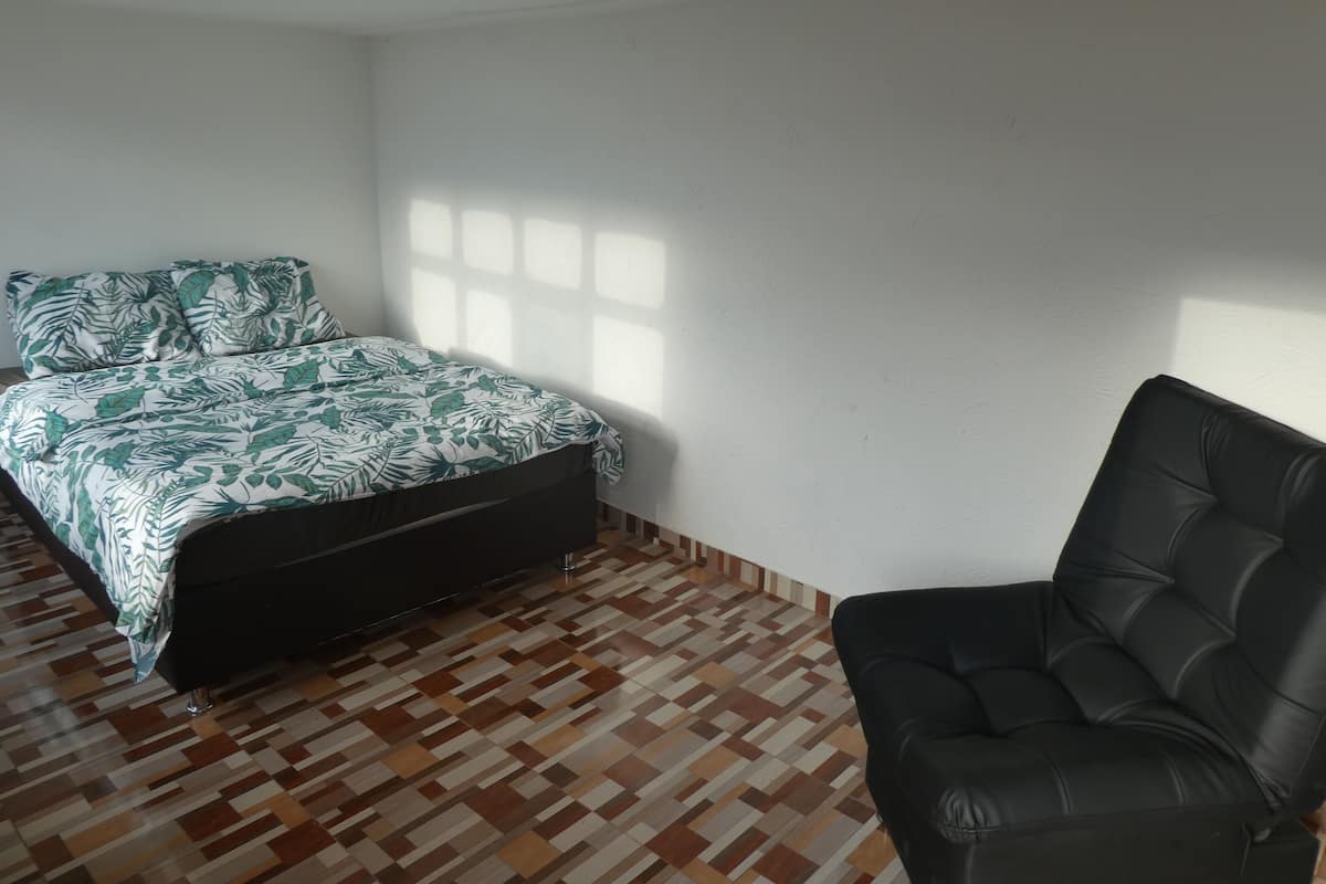 A bedroom with a bed, a black leather chair, and a patterned bedspread.