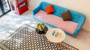 A room with a blue sofa, a small round table with drinks, and a Coca-Cola refrigerator. - The Poppy Villa & Hotel (Hanoi)
