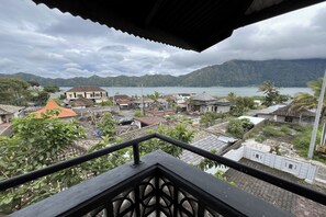 Une vue depuis un balcon donnant sur une ville côtière, avec des maisons, une étendue d’eau et des montagnes en arrière-plan.