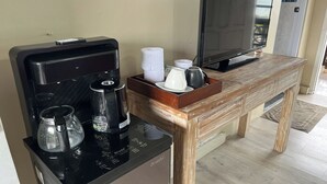 Un espace de vie compact comprenant une machine à café, une verseuse en verre, une télécommande, un téléviseur et une petite table en bois.