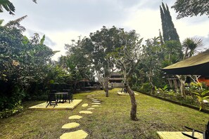 Un jardín con un sendero pavimentado, mobiliario exterior y diversas plantas.