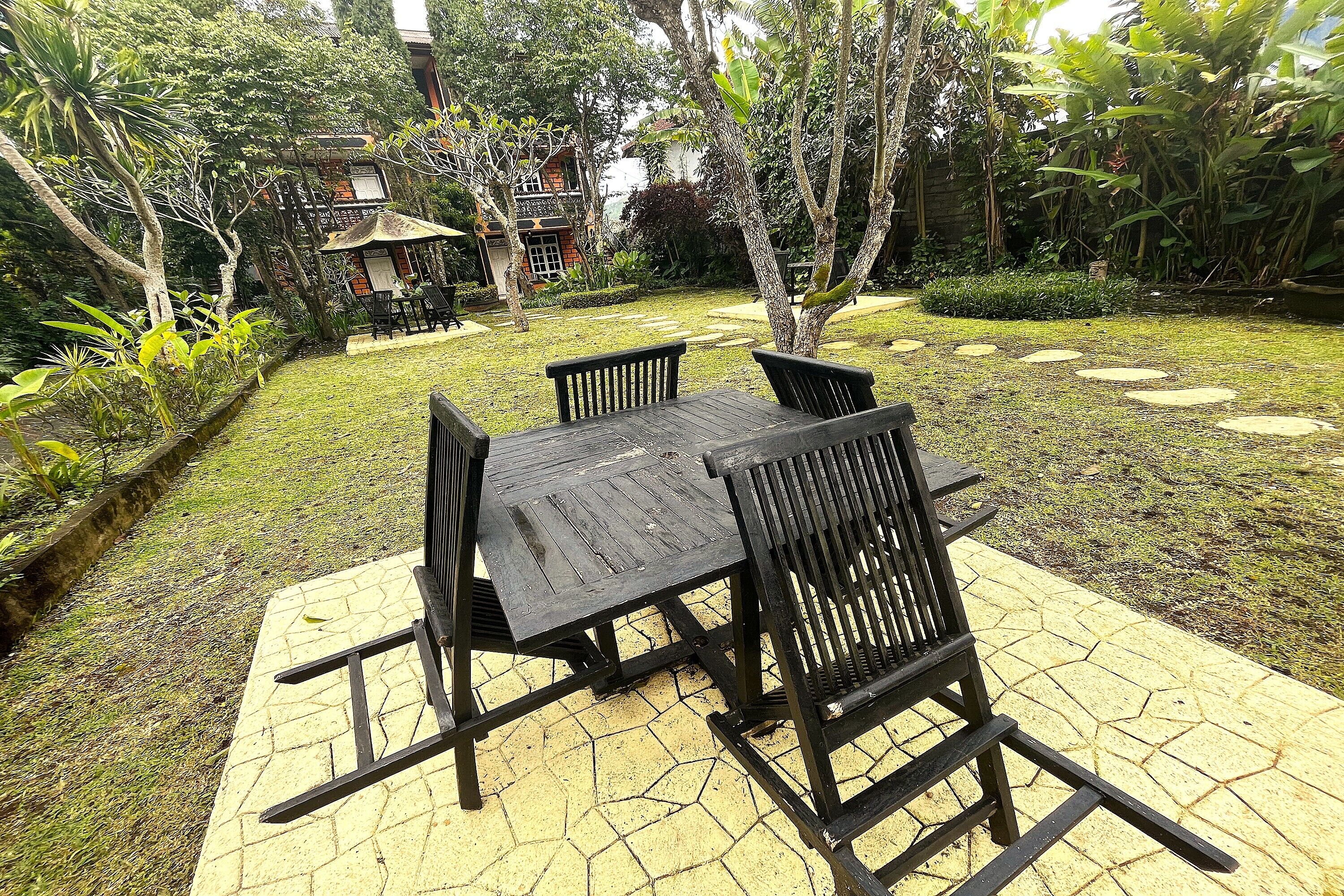 A garden patio with a table and chairs, surrounded by lush greenery and a small pond.