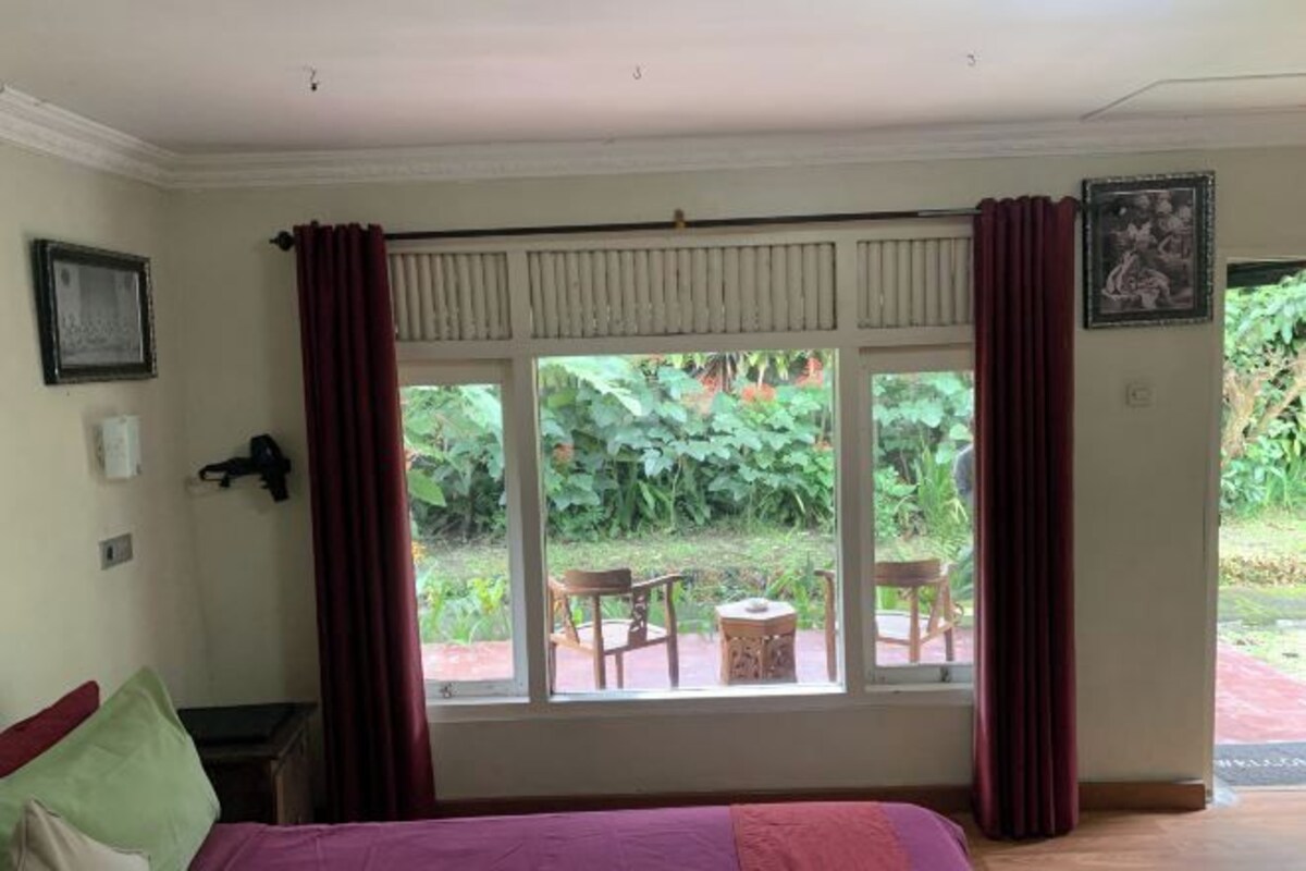 A room with a bed, a window with curtains, a chair, and a small table.